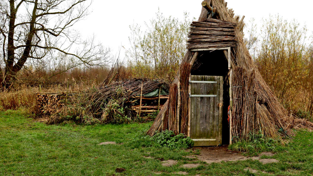 Hut van riet en wilgentakken in het gras bij het Biesbosch Museum